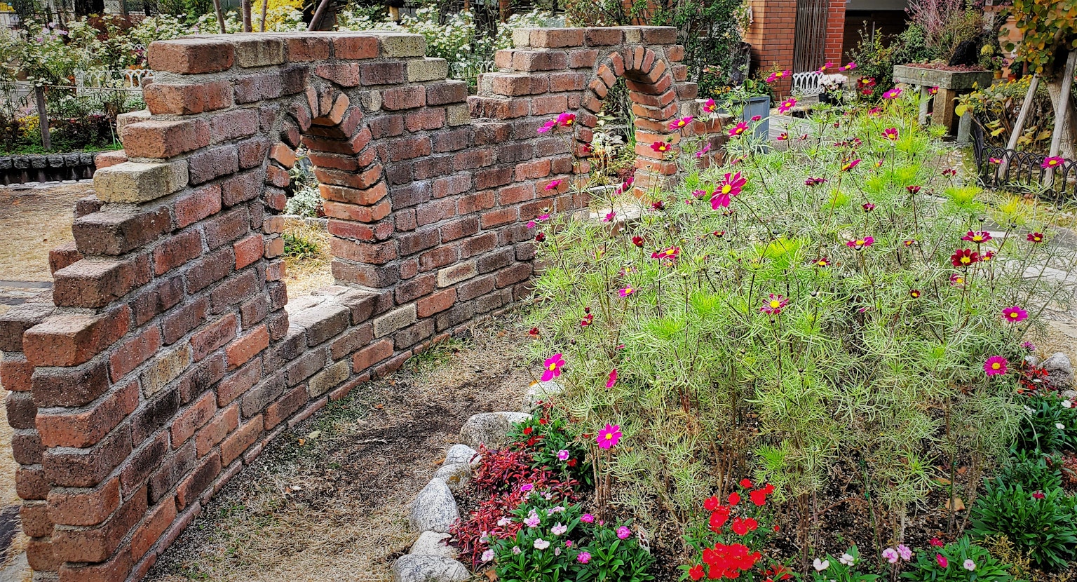 Ziegelbogenwand umgeben von bunten Blumen in einem Garten