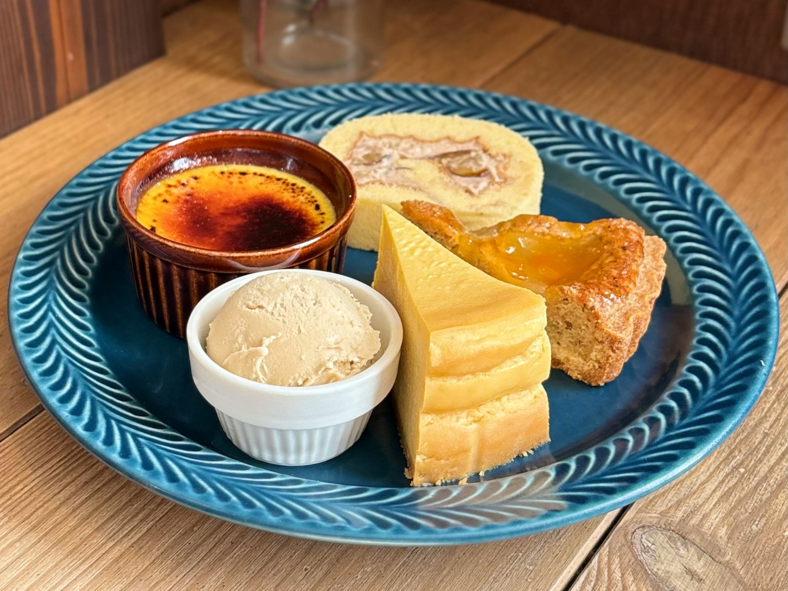 A dessert platter featuring crème brûlée, ice cream, cheesecake, and scone on a blue plate