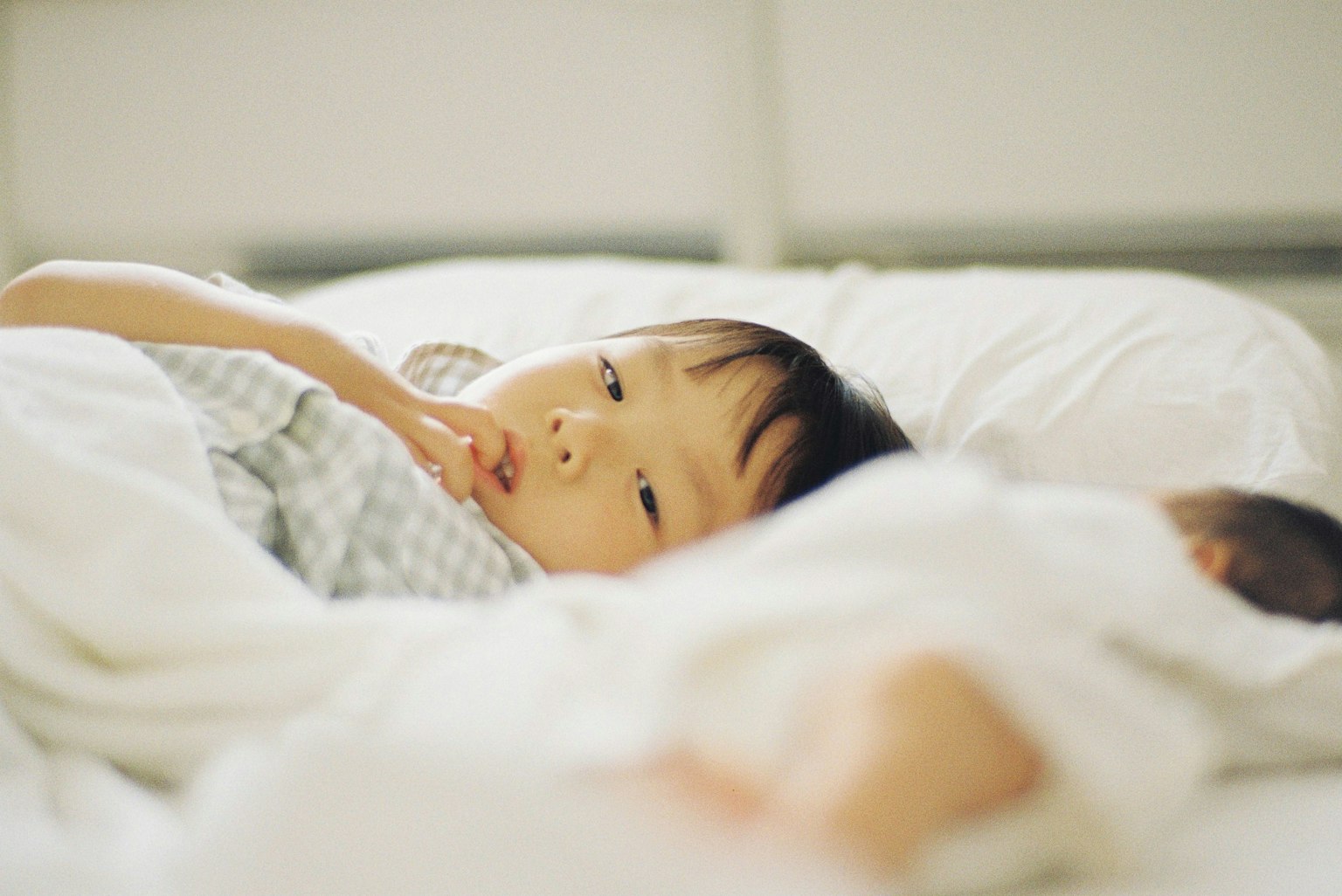 ベッドに横たわる子供の穏やかな表情と白い布団