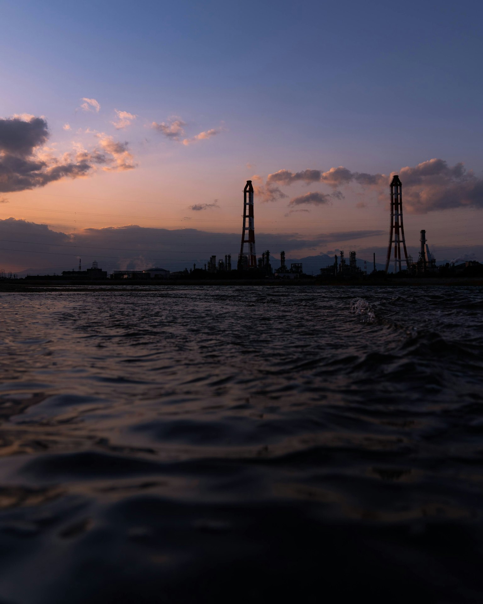 夕暮れ時の水面と工業用塔のシルエット