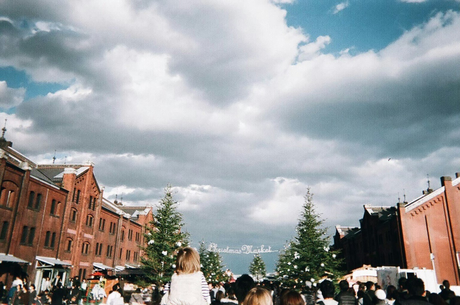 Crowd gathered in a square with red brick buildings and Christmas trees