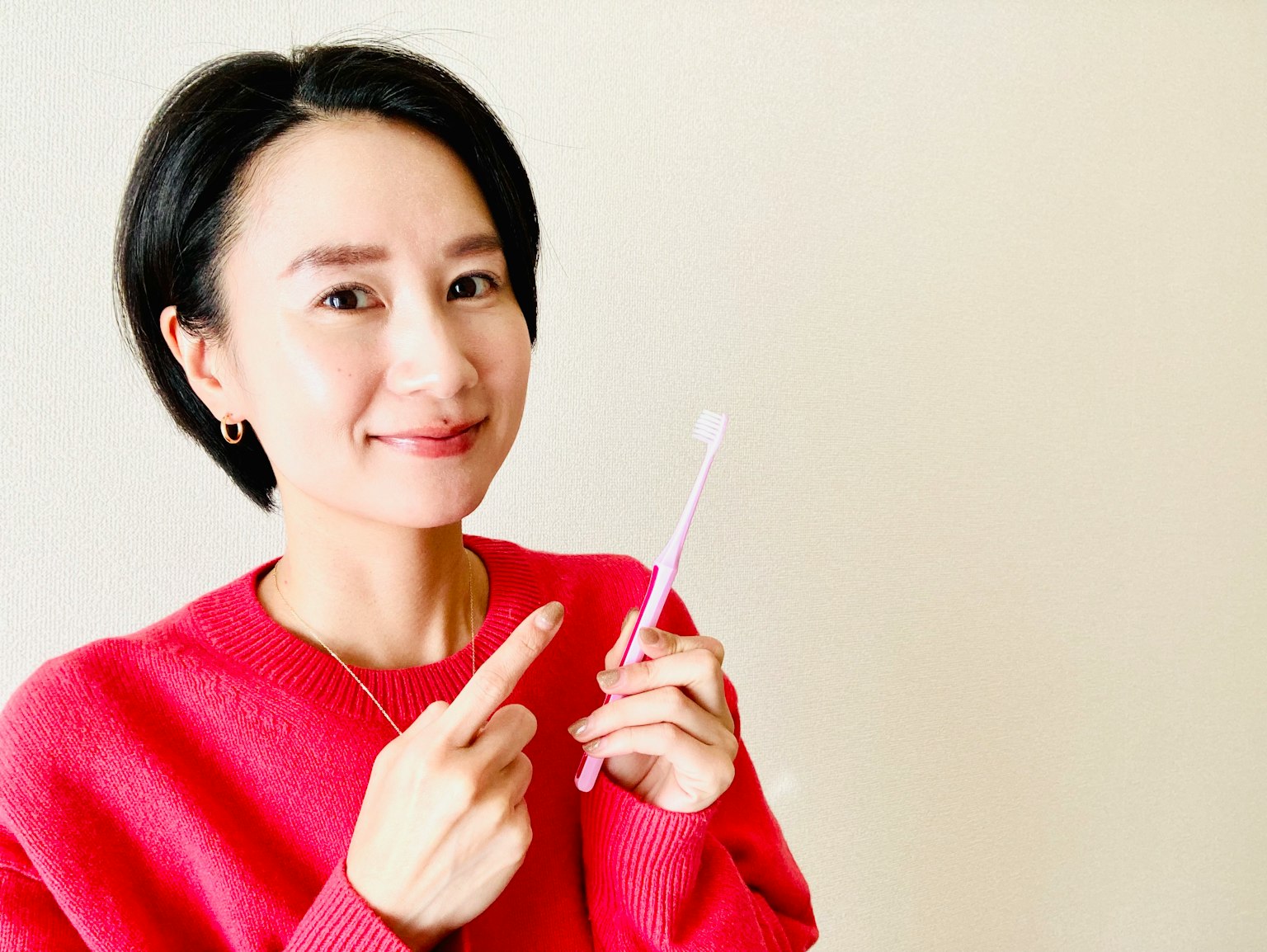 Una donna che indossa un maglione rosa sorridendo mentre tiene uno spazzolino
