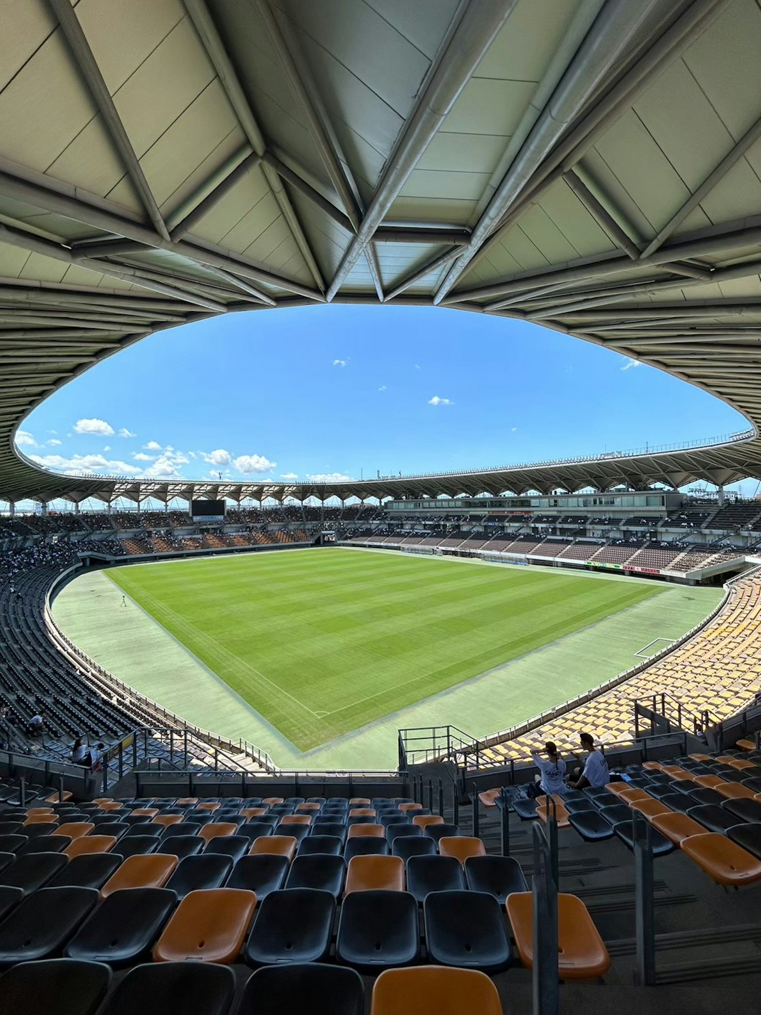 Vista di uno stadio spazioso con un campo verde e cielo blu dall'area dei posti a sedere
