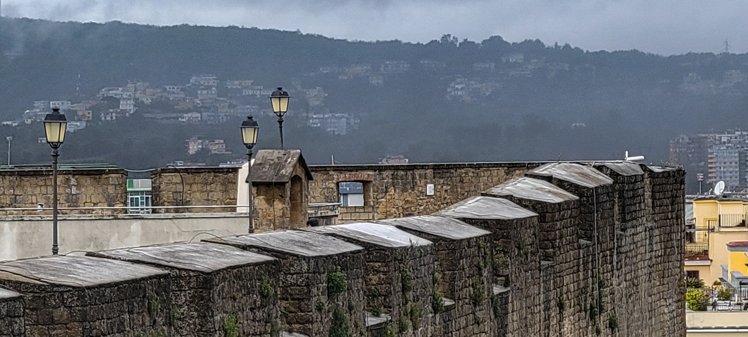 Blick auf eine Steinmauer mit Straßenlaternen und fernen Bergen