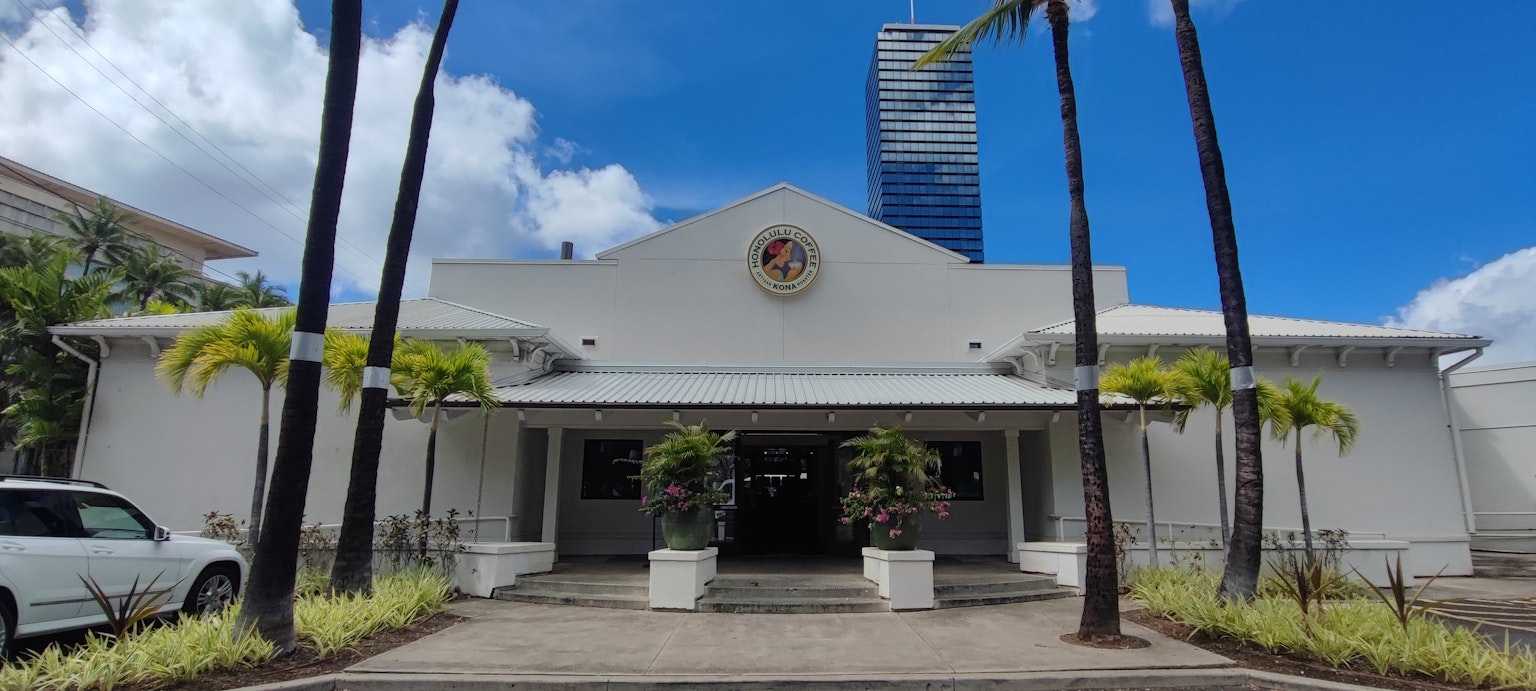 Vista exterior de un edificio blanco bajo un cielo azul con palmeras