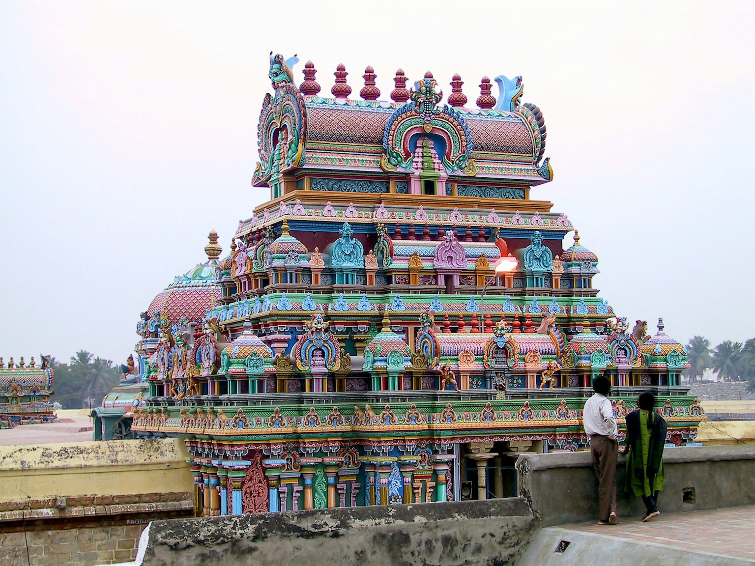 Esterno di un tempio del sud dell'India decorato in modo vivace al crepuscolo con due persone nelle vicinanze