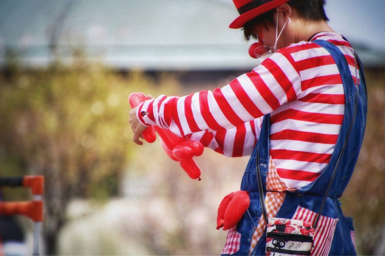 戴红白条纹服的孩子小丑在户外活动中拿着红色气球