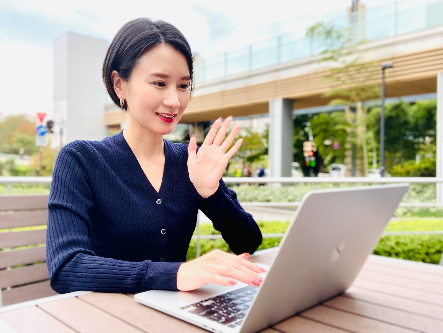 Eine Frau winkt, während sie in einem Park einen Laptop benutzt