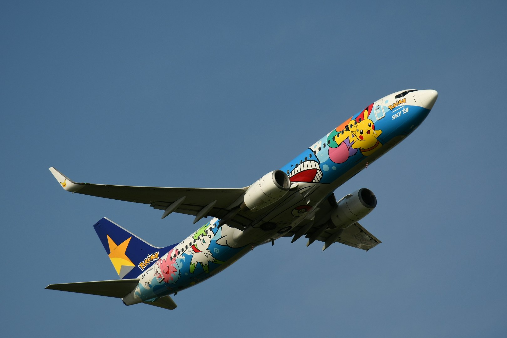 青空を飛ぶカラフルな旅客機の機首と翼