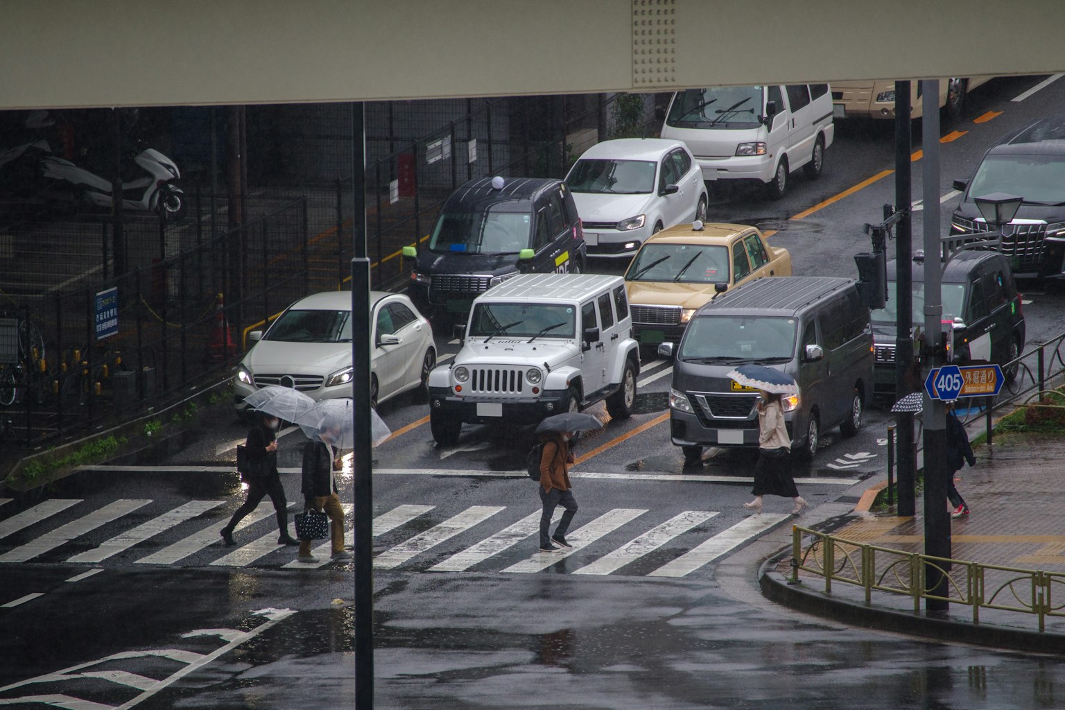 People crossing the street in the rain with cars passing nearby