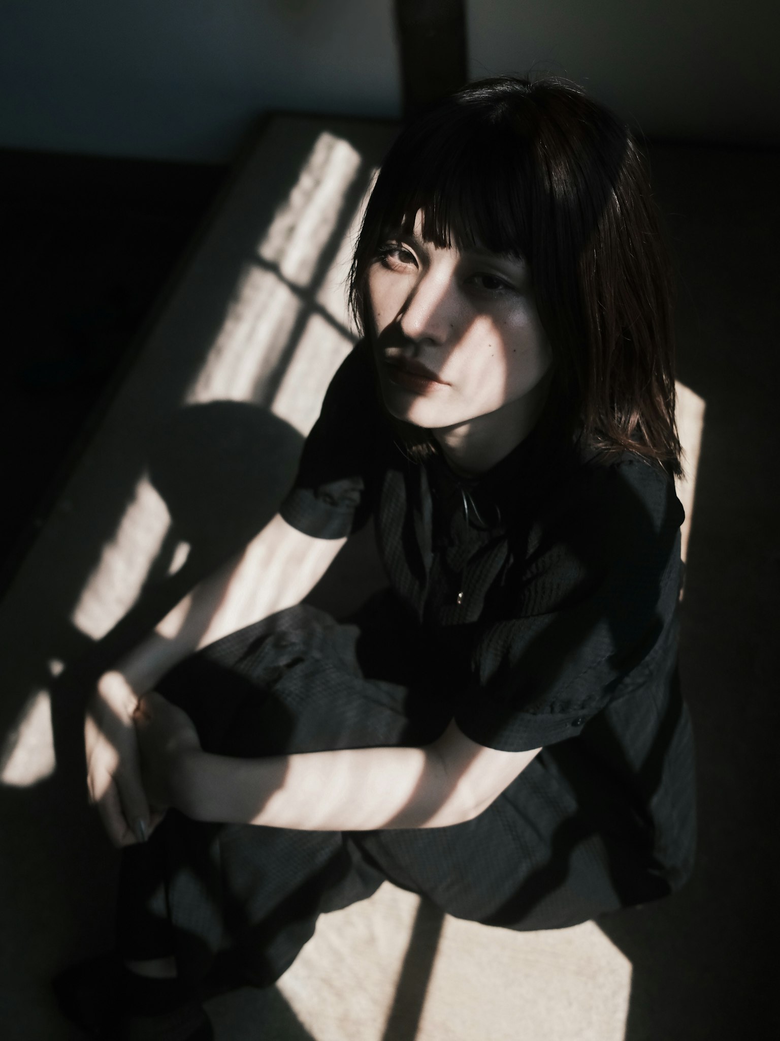 影の中に座る女性のポートレート 黒い服を着ている 窓からの光が影を作り出している