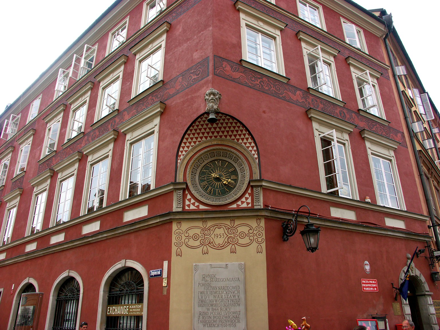 Angolo di un edificio con facciata rossa caratterizzato da un orologio decorativo e una scultura