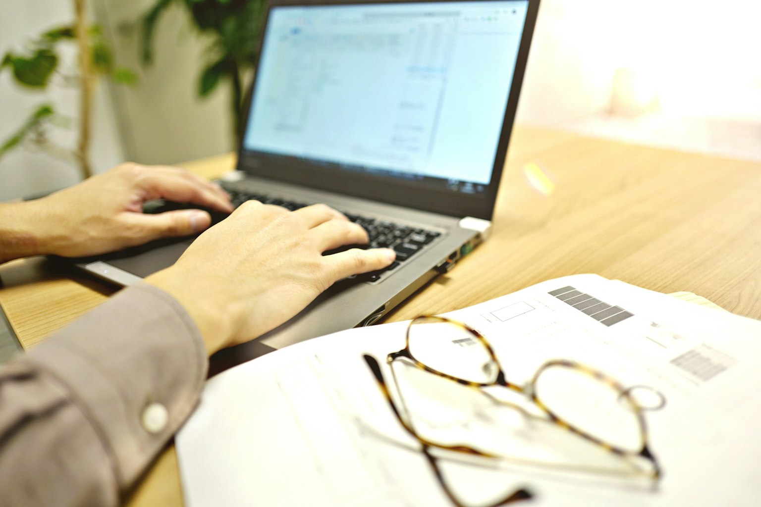 Nahaufnahme von Händen, die auf einem Laptop tippen, mit einem ordentlich organisierten Schreibtisch und einer Brille