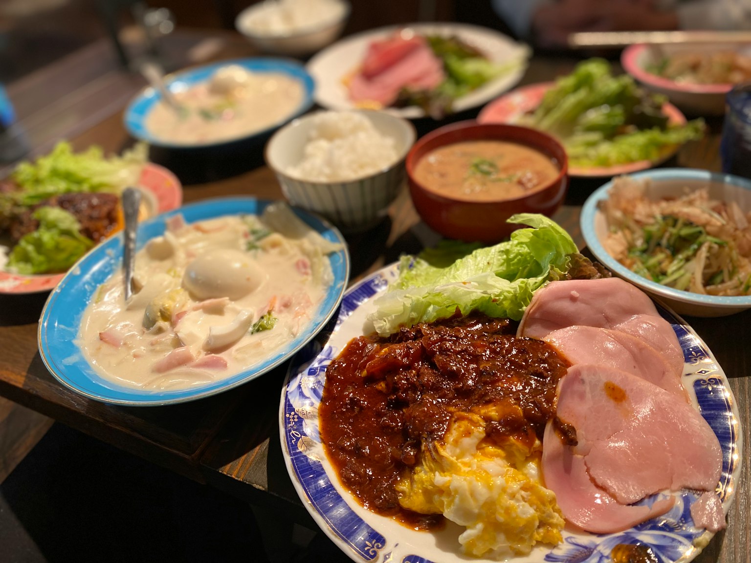 Một bàn đầy những món ăn nhiều màu sắc bao gồm món trứng, giăm bông, salad, cơm và súp