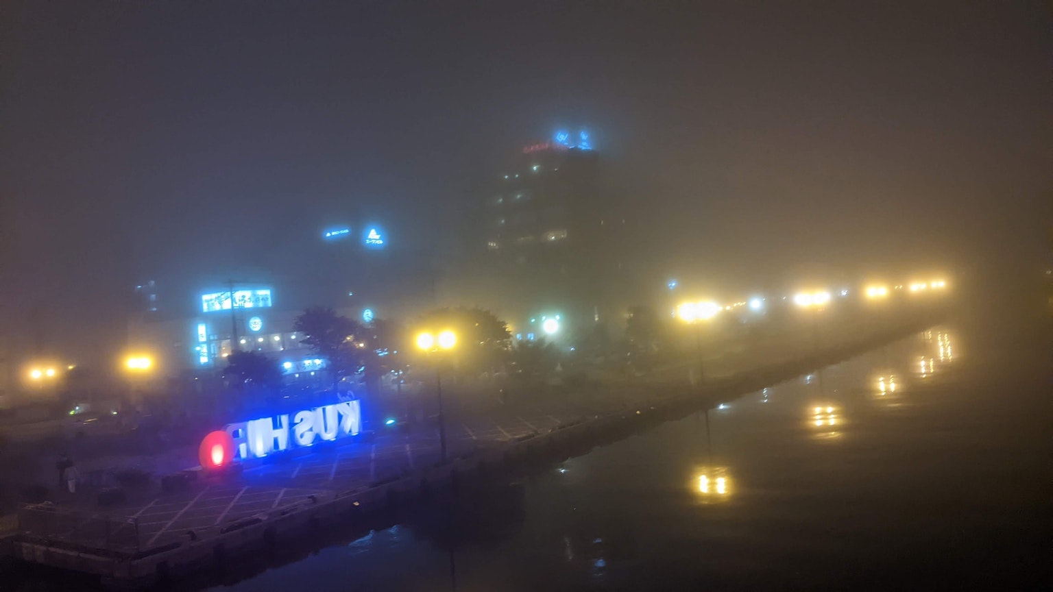 Paesaggio urbano notturno avvolto nella nebbia con insegne al neon e lampioni illuminati