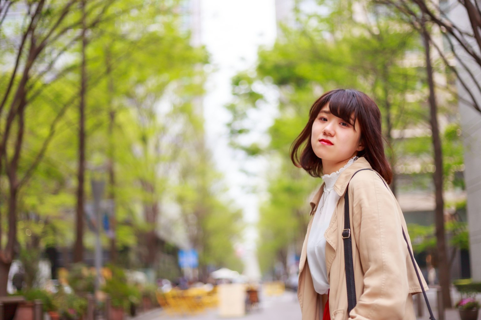 春天在樹木成行的街道上行走的年輕女性