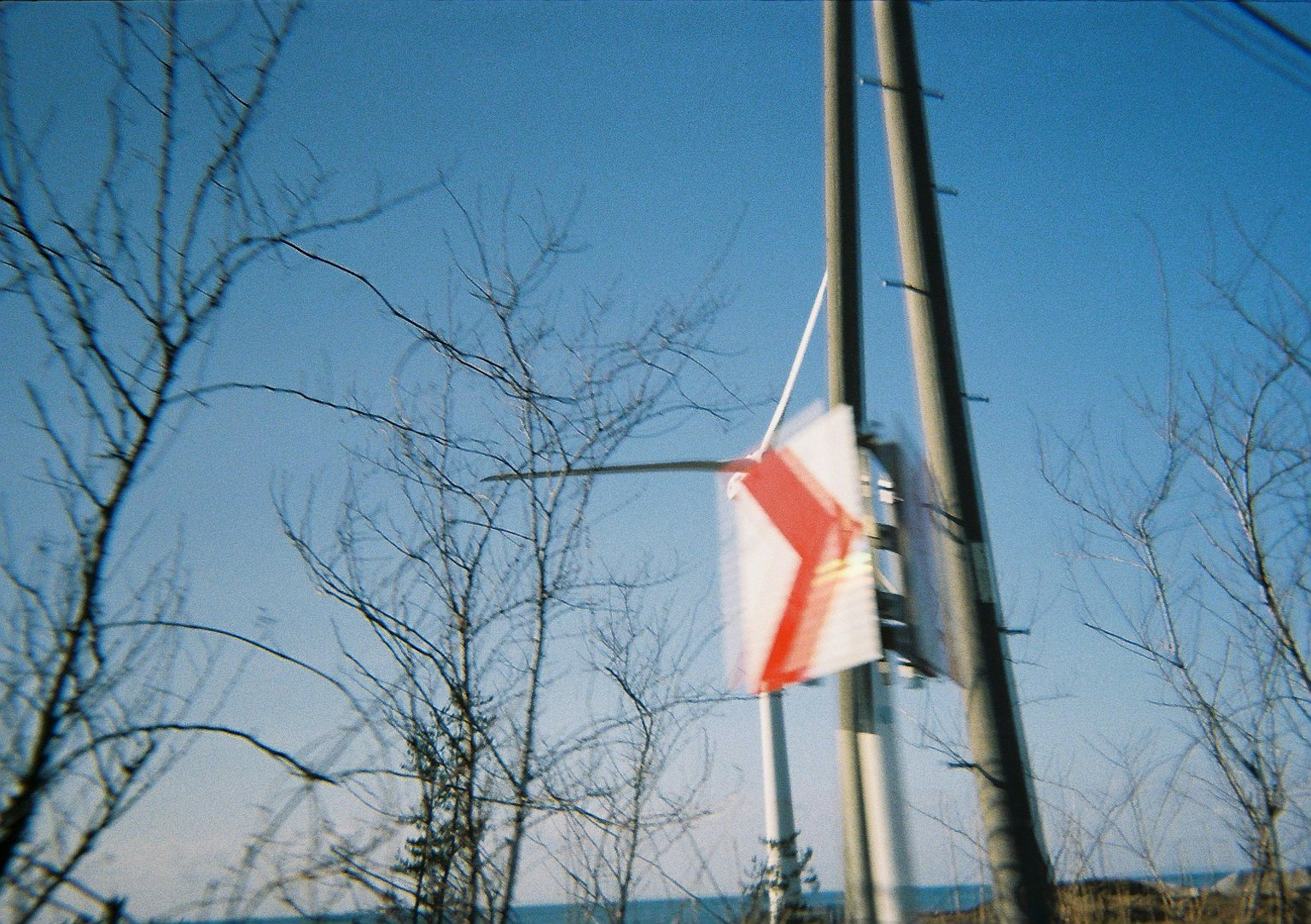 Eine Flagge mit einem roten Kreuz, die an einem Pfosten vor einem klaren blauen Himmel hängt