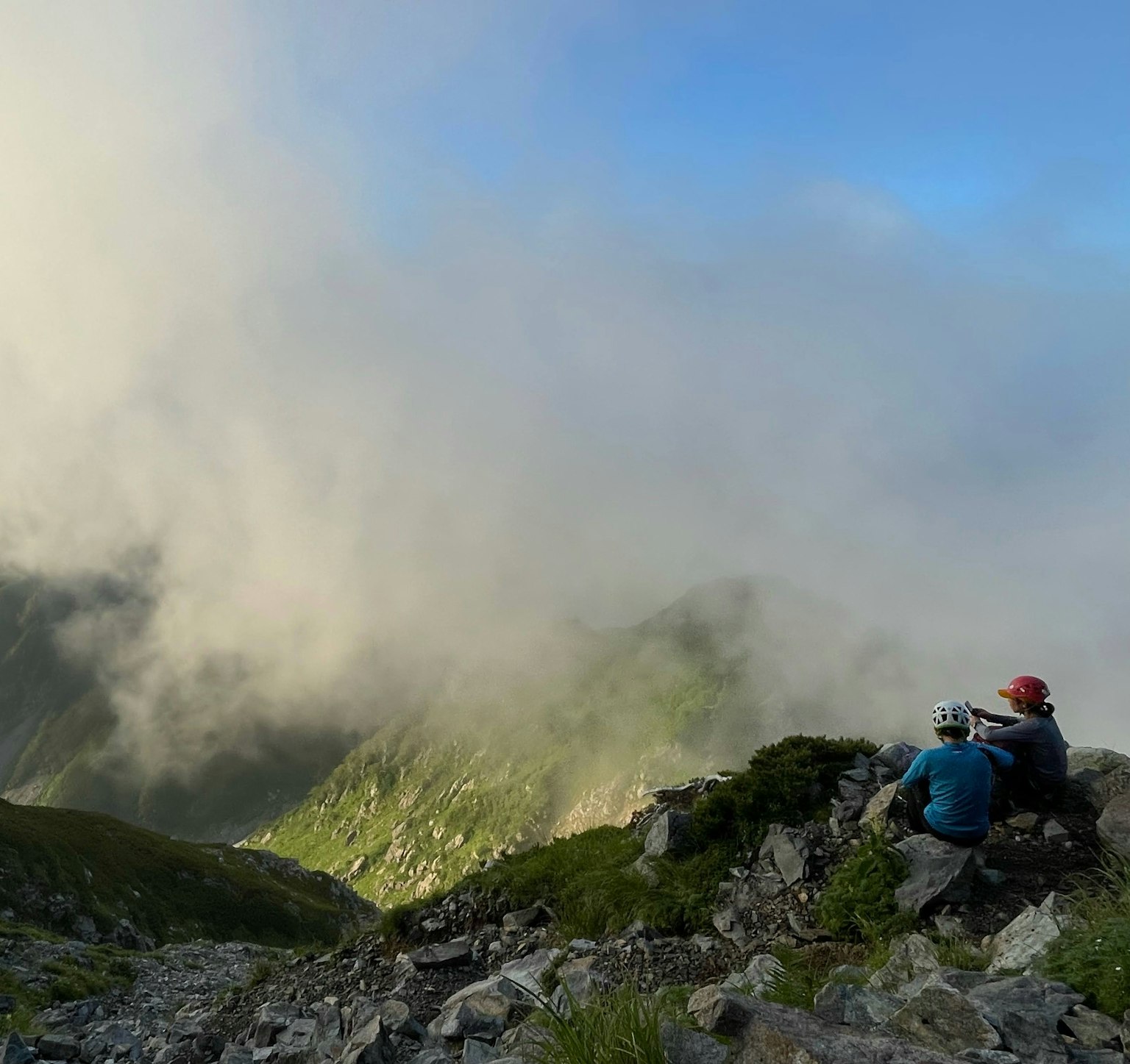 两名登山者坐在岩石坡上，观看笼罩在雾中的山