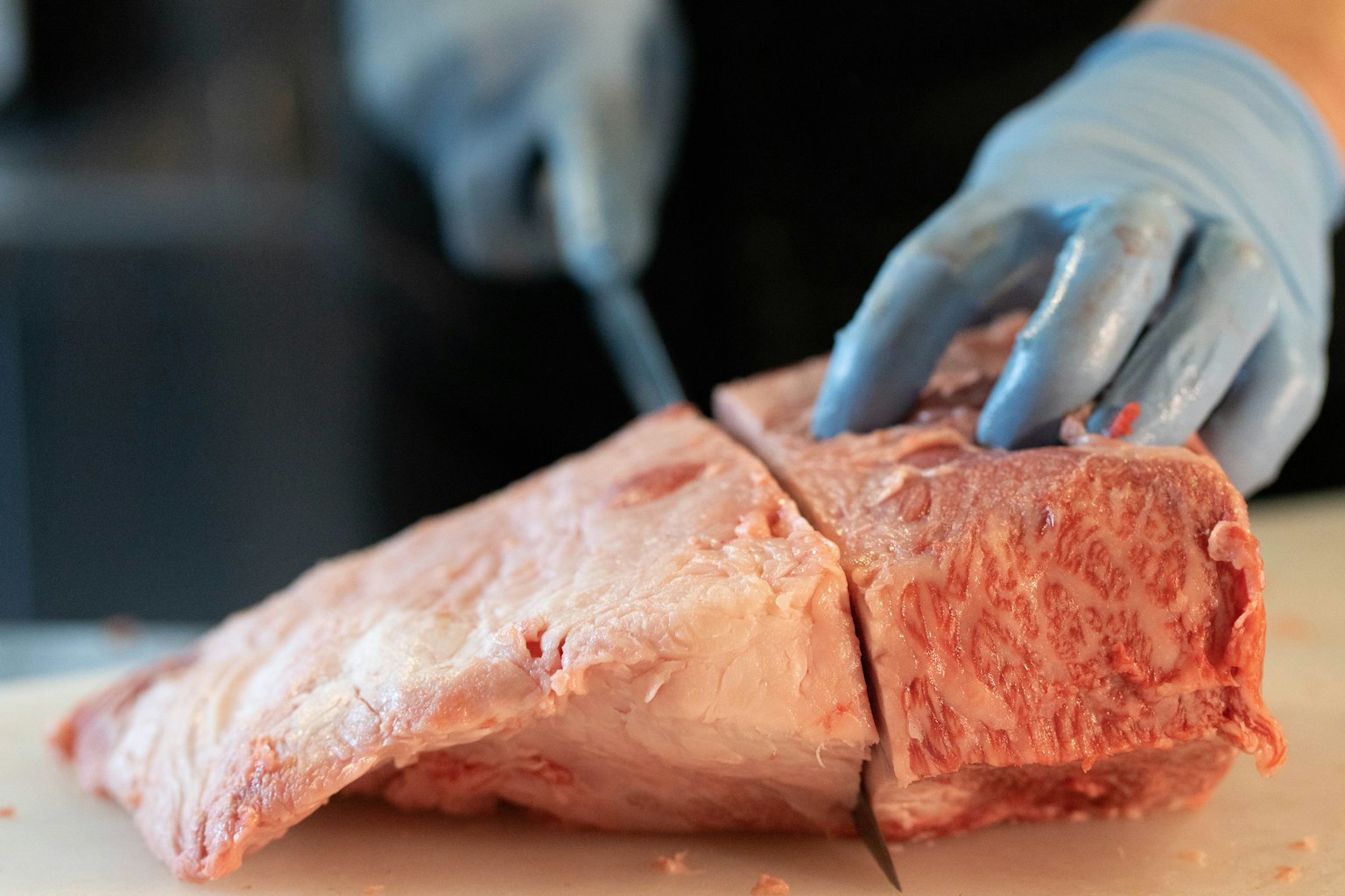 Nahaufnahme von Händen mit blauen Handschuhen, die Fleisch schneiden