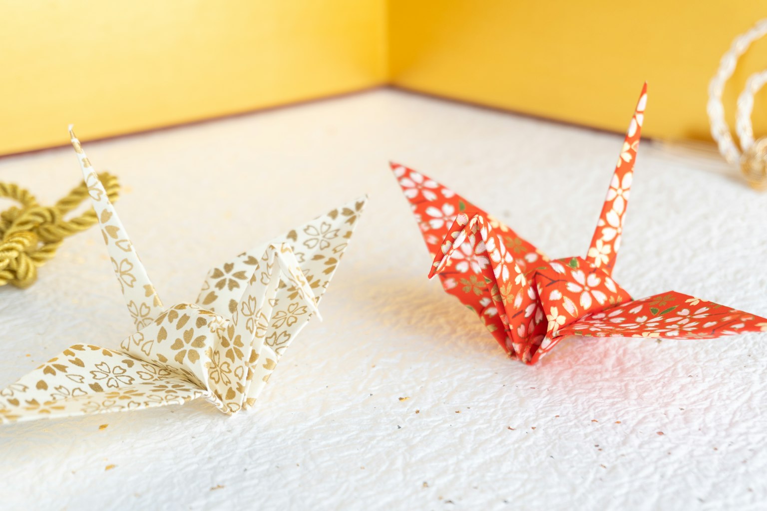 Weiße und rote Origami-Kraniche auf einem gelben Hintergrund