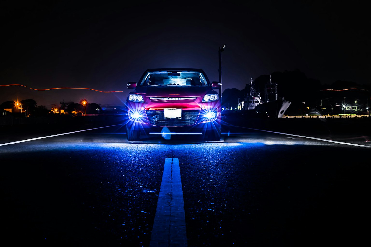 Vista frontal de un coche rojo en una carretera nocturna con luces azules brillantes