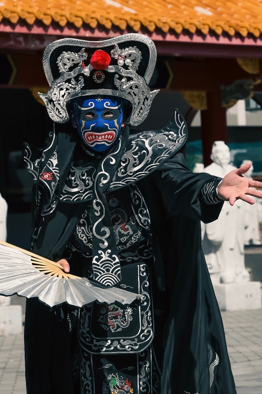escena al aire libre: intérprete con máscara negra y abanico abierto