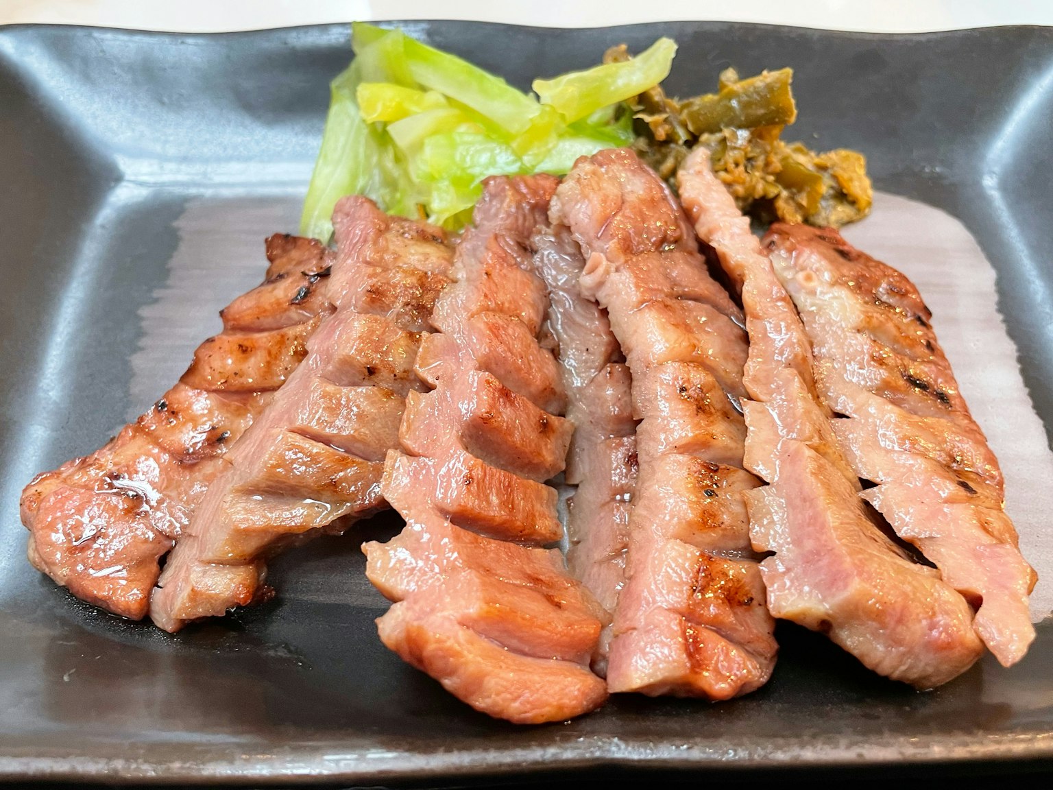 Miếng thịt nướng được phục vụ trên đĩa đen với rau xanh