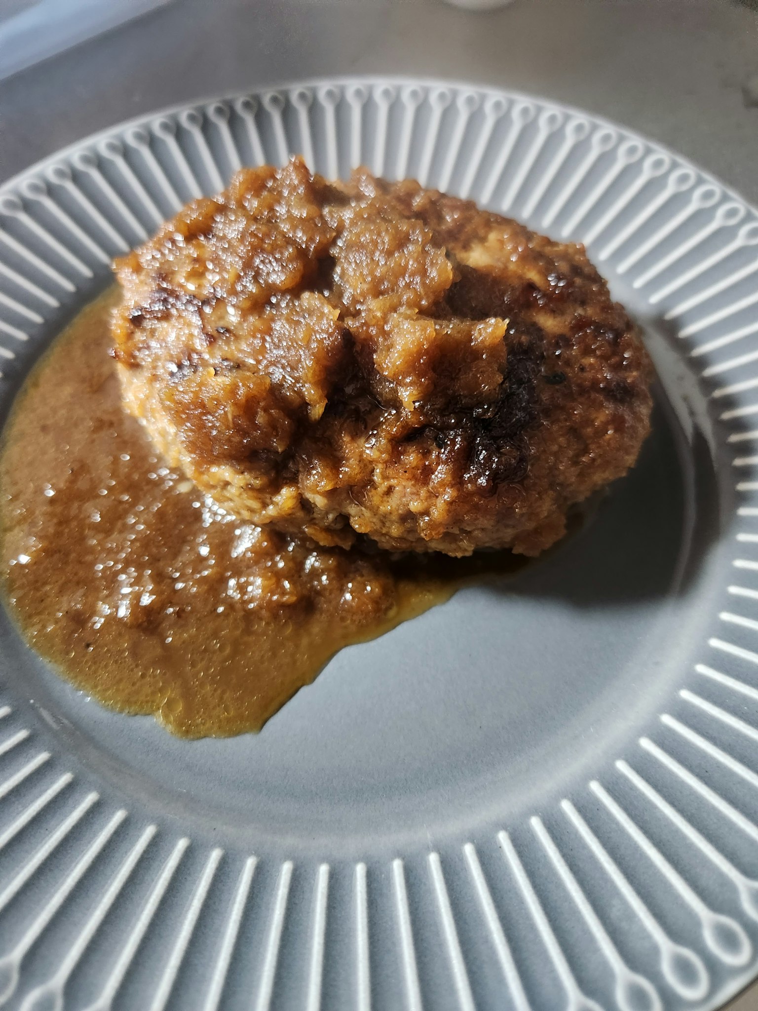 Un steak haché doré avec une sauce gravy sur une assiette décorative