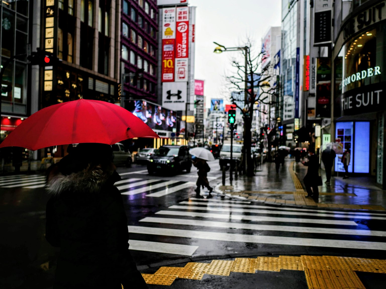 People with red umbrellas crossing a street in the rain surrounded by buildings