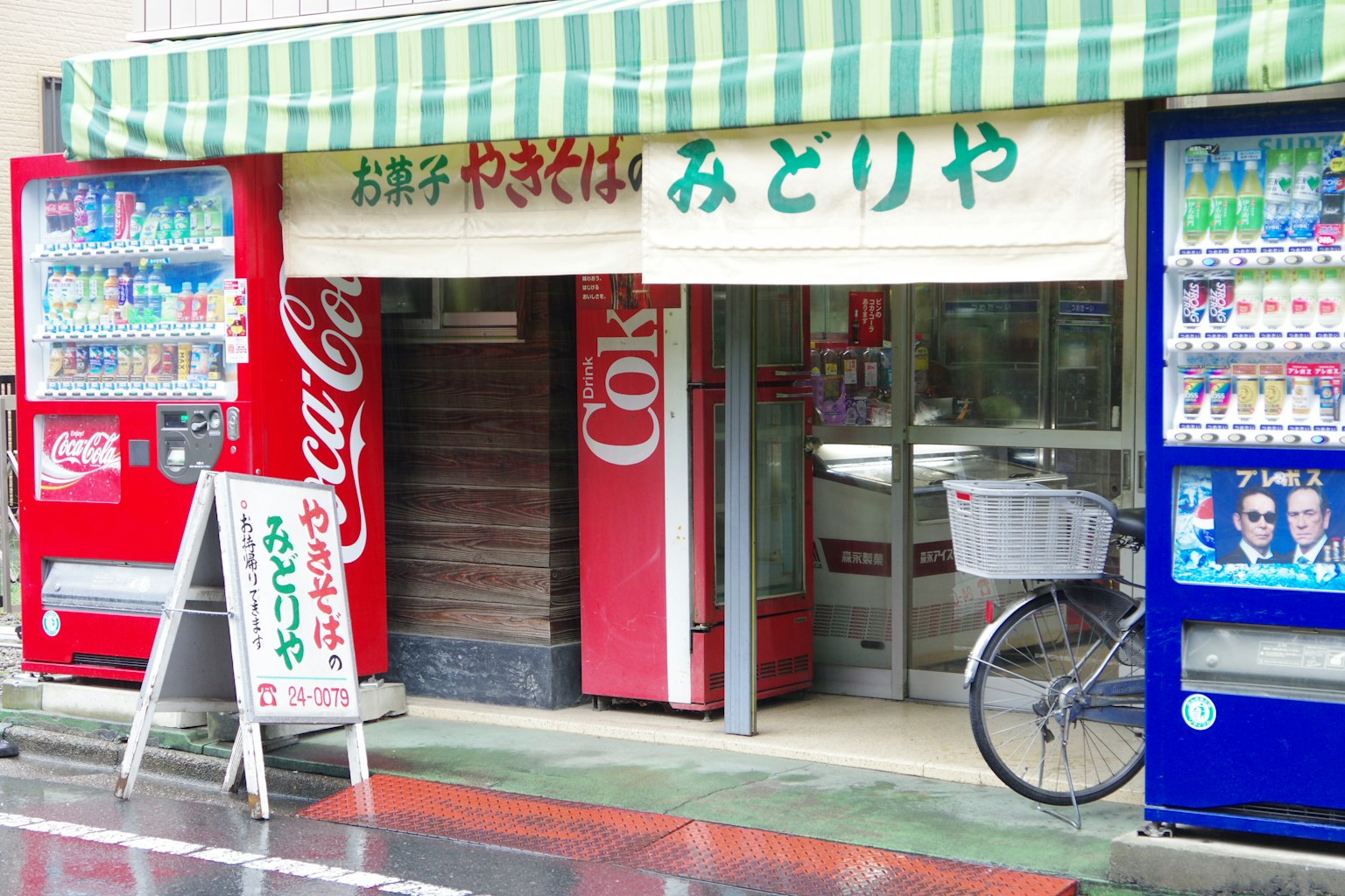 Esterno di un piccolo negozio Midoriya con distributori automatici e una bicicletta
