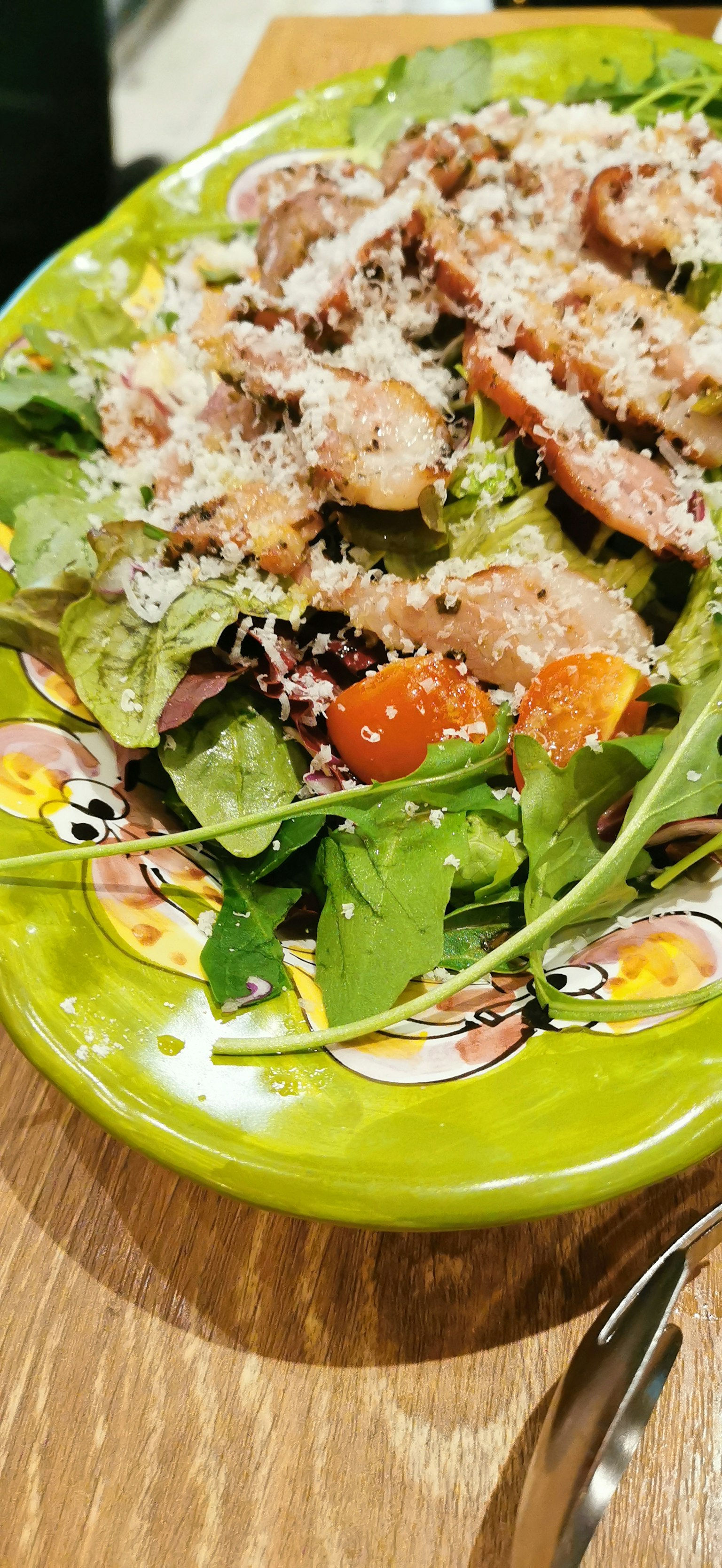 Ensalada en un plato verde cubierta con queso parmesano y tomates