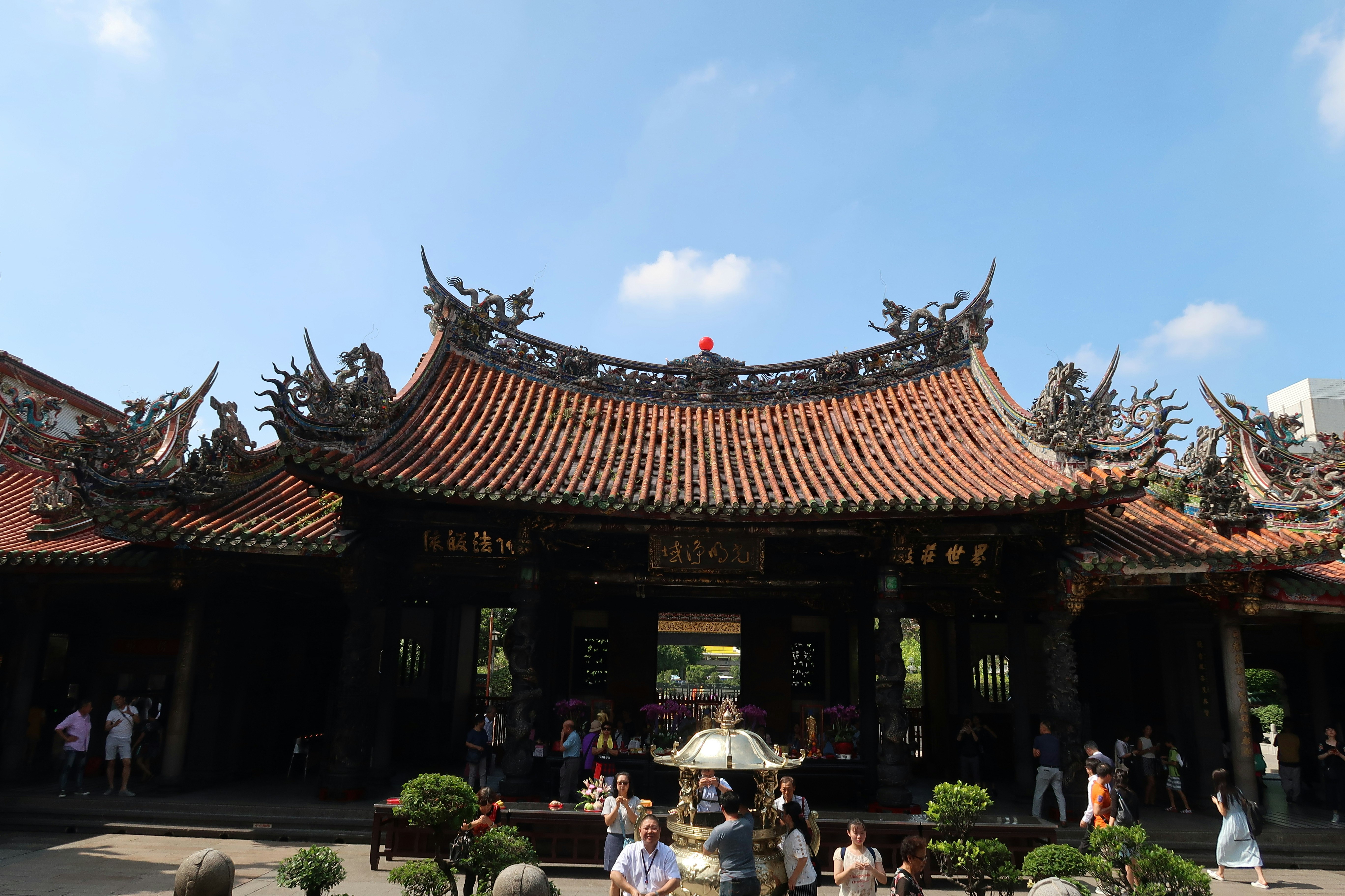 台湾の寺院の朱塗りの大殿と参拝者のいる中庭