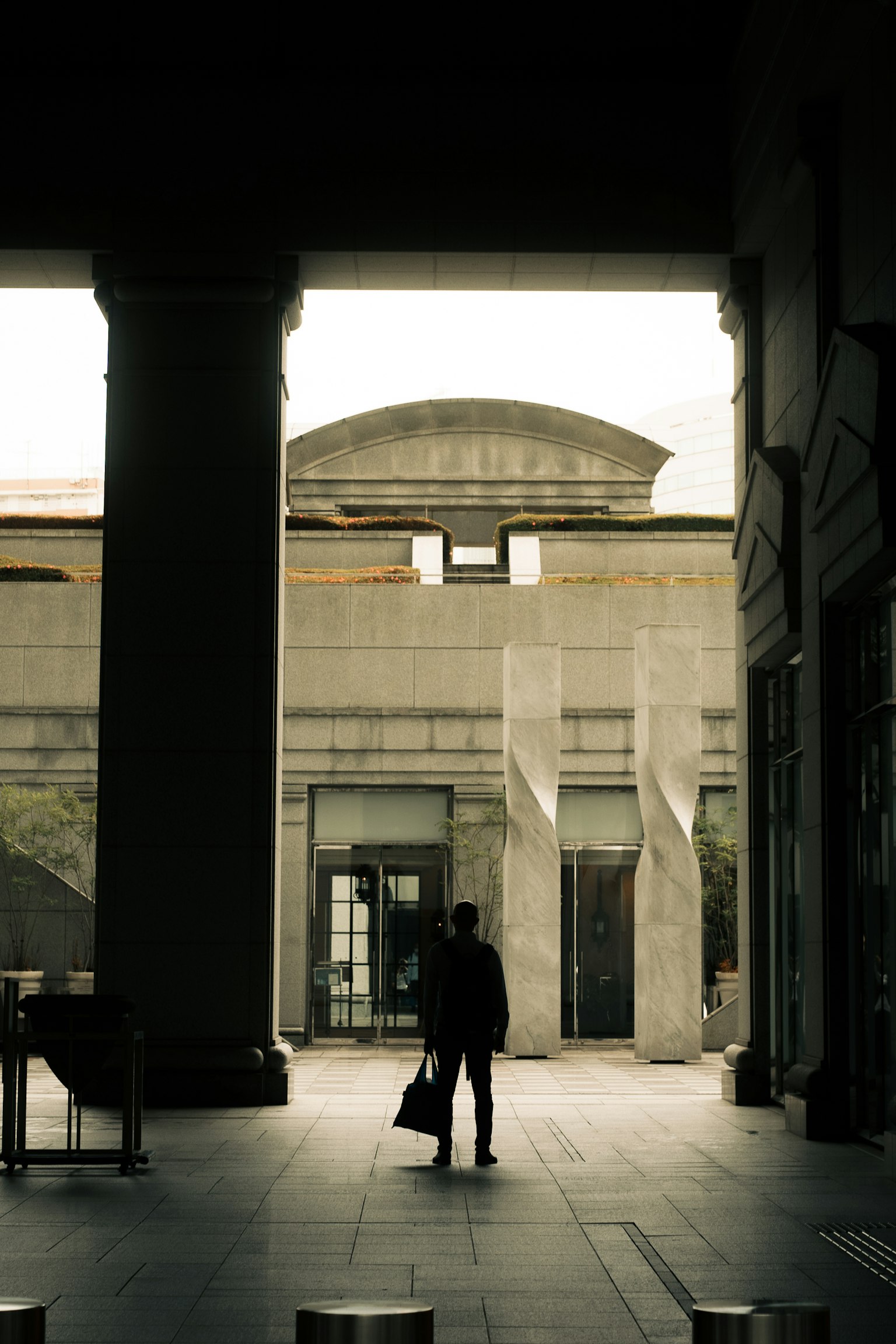 Silueta de una persona de pie entre columnas de concreto con esculturas modernas dentro de un edificio