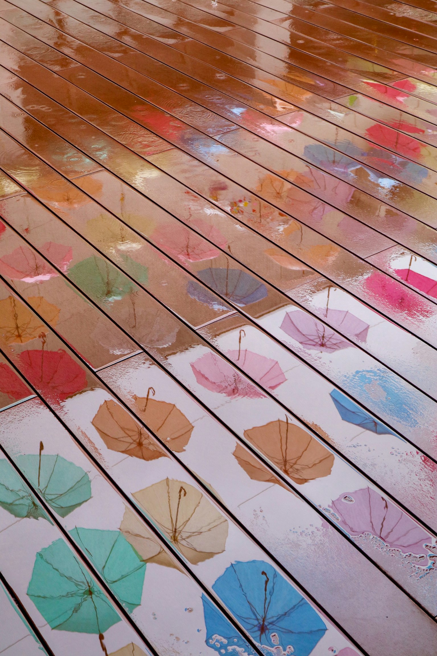 Colorful umbrellas on the floor with reflections on wooden planks