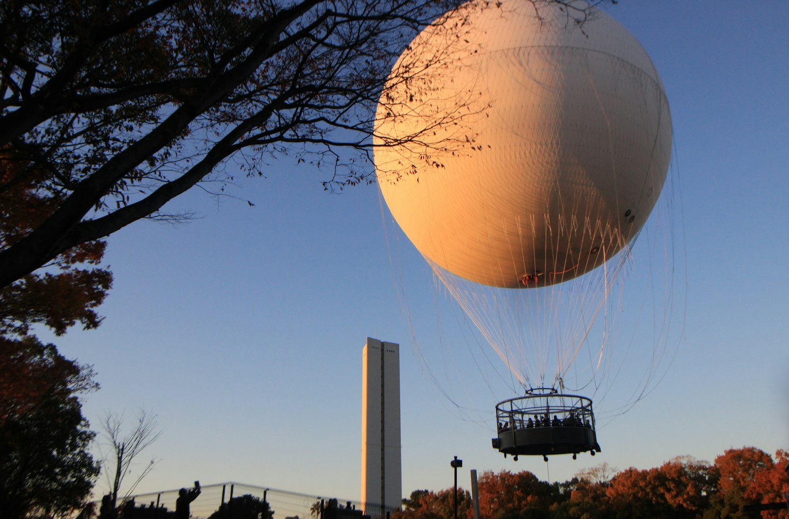 บอลลูนขนาดใหญ่ลอยอยู่ในสวนพร้อมกับรถกอนโดลาที่อยู่ใต้ท้องฟ้าสีส้มในยามพระอาทิตย์ตก