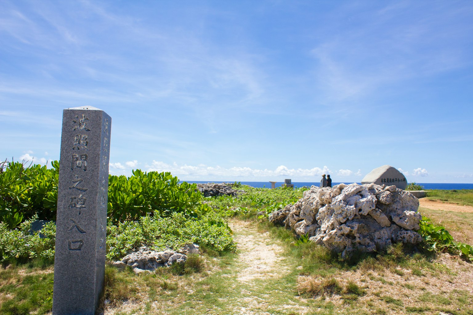 Vista escénica con un monumento de piedra y un camino rocoso que lleva al océano bajo un cielo azul
