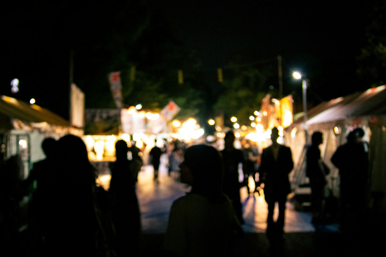 夜の祭りの雰囲気を持つ人々のシルエットと明るい屋台の光