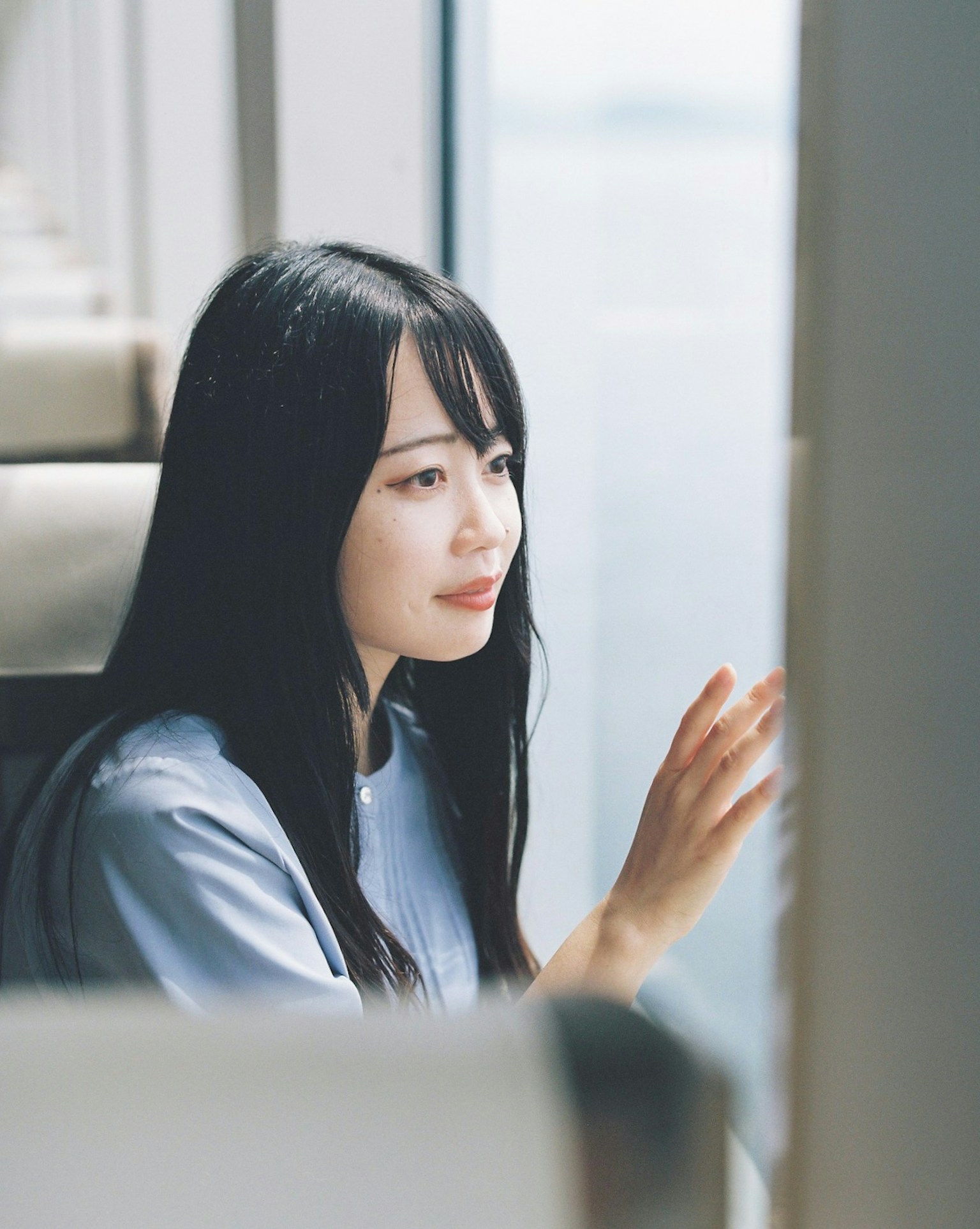 侧面看一位女性在窗外凝视，长黑发，穿着蓝色衬衫