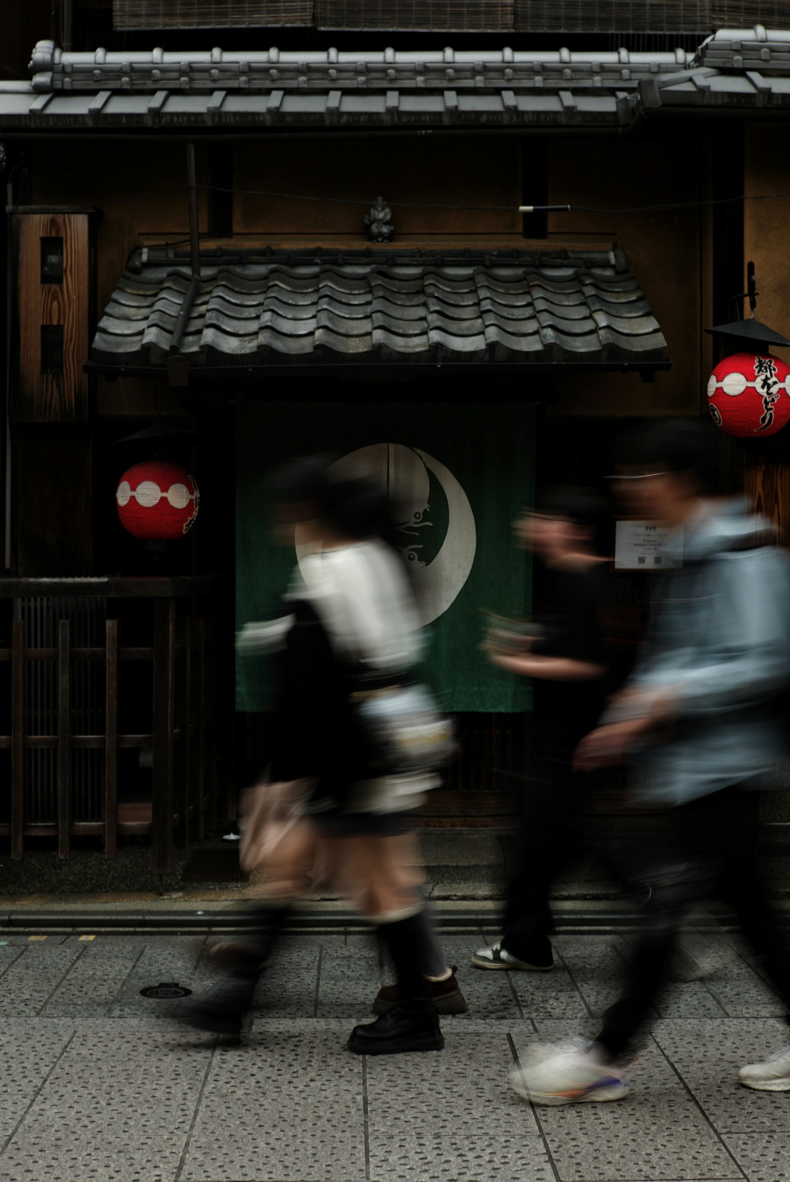 人々が通り過ぎる伝統的な日本の建物と赤い提灯