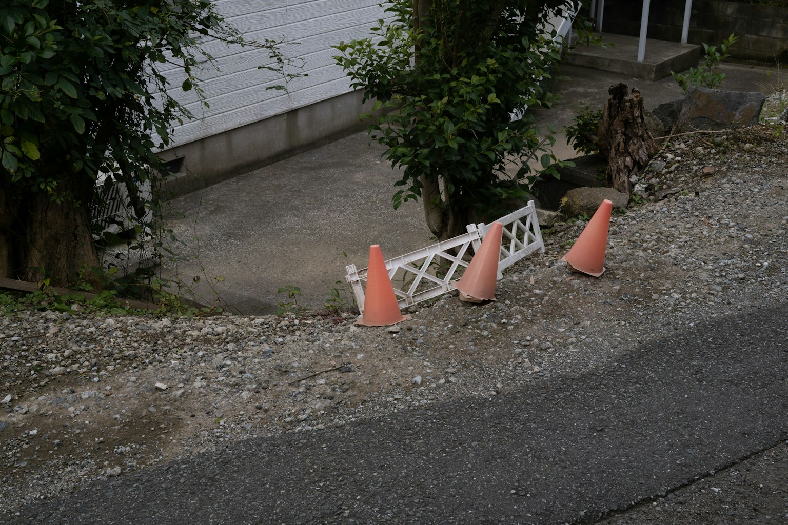 Scene featuring orange traffic cones and a white fence by the roadside
