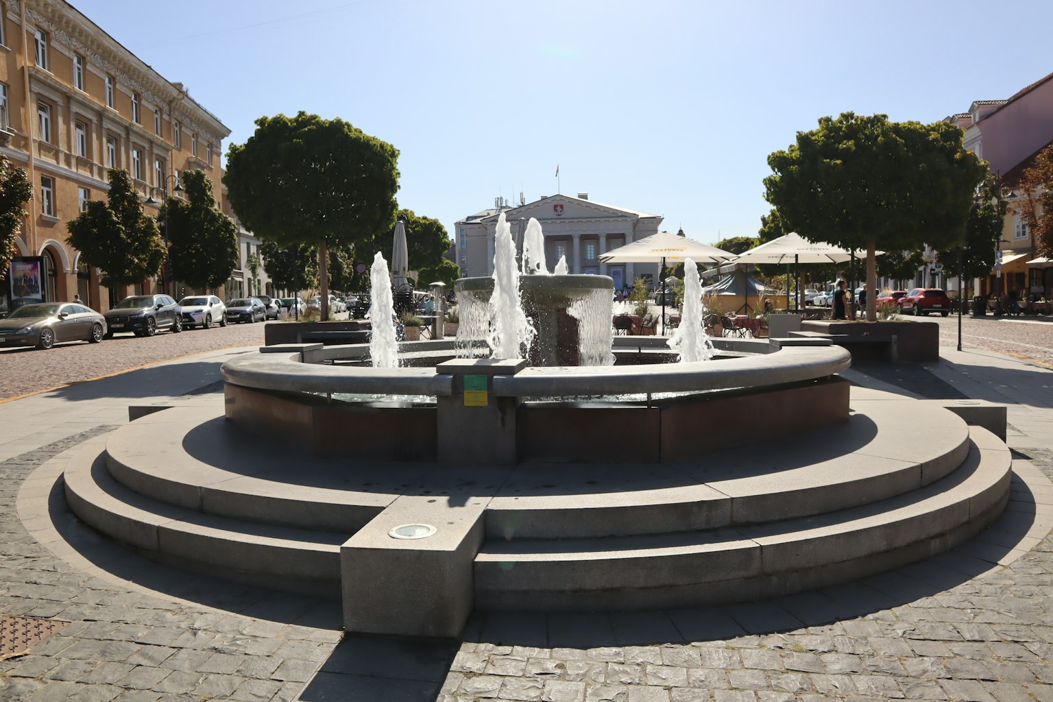 Fontana circolare in una piazza circondata da alberi e posti a sedere all'aperto
