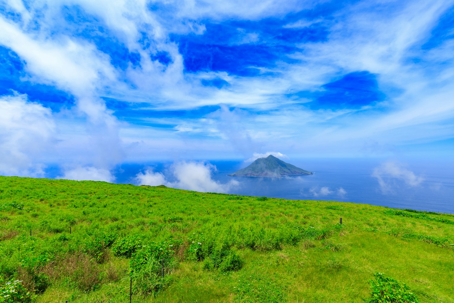 郁郁葱葱的草地在明亮的蓝天和云朵下，远处有一座火山