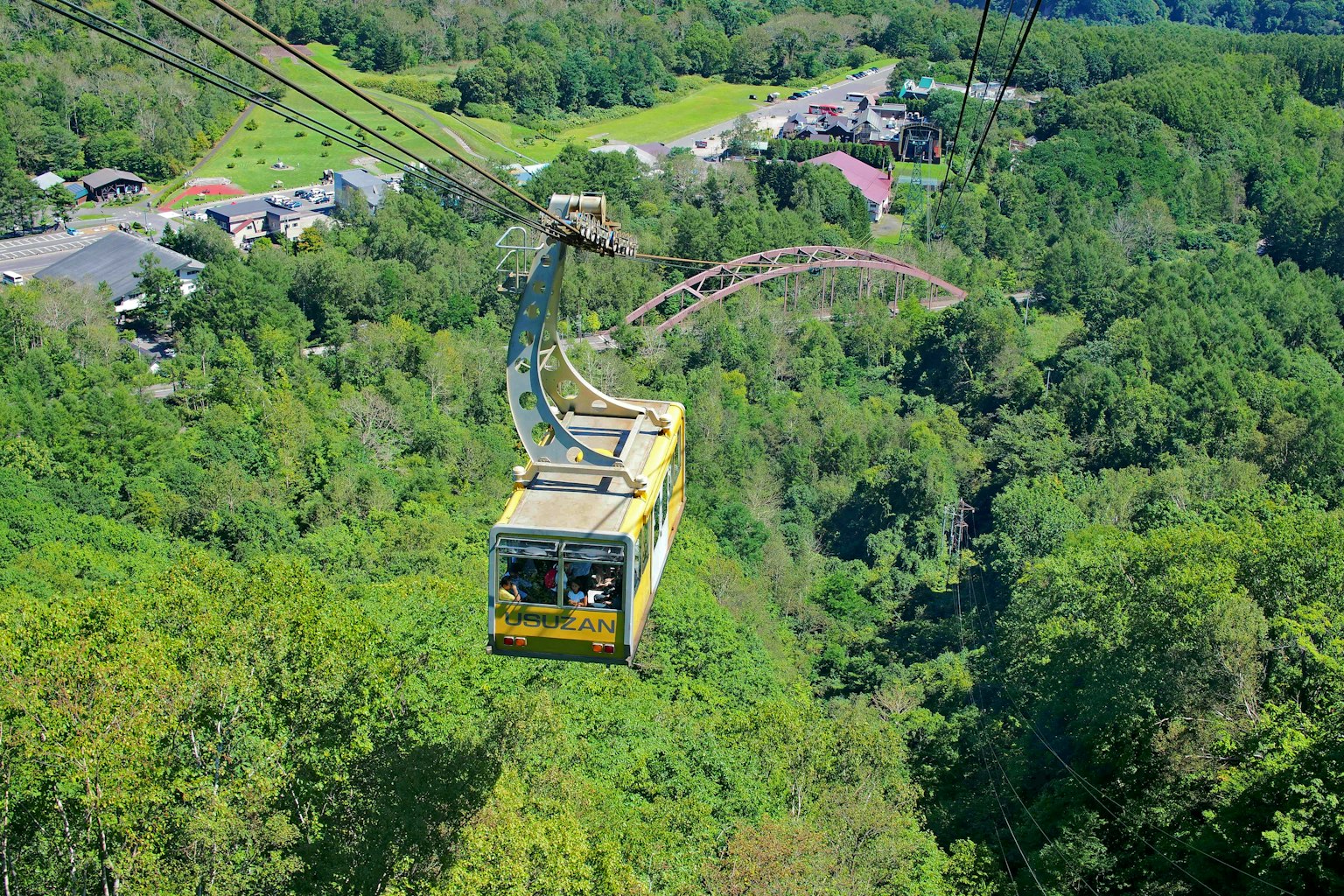 A cable car traveling through lush green mountains with surrounding scenery