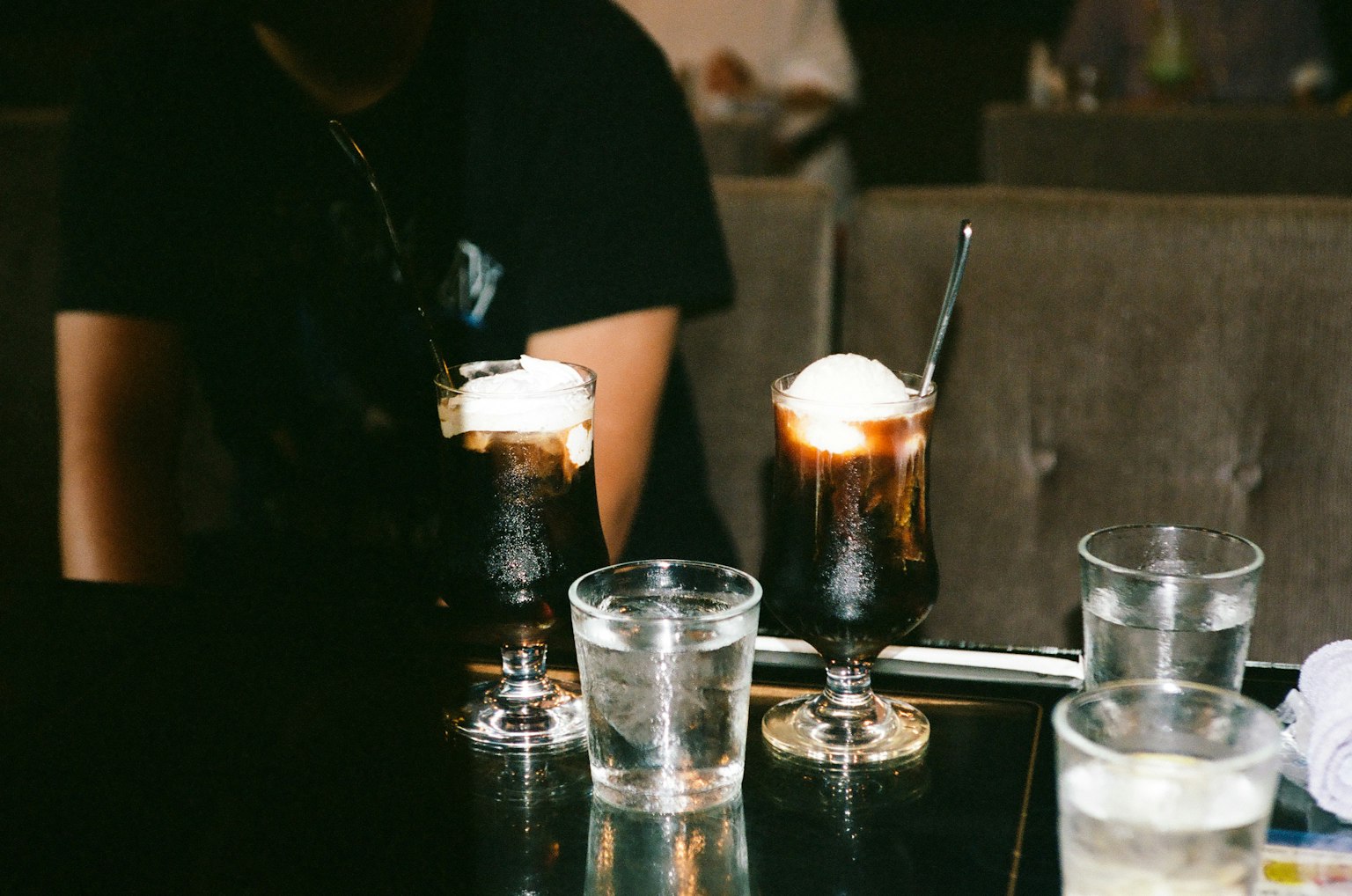 Two glasses of iced coffee with ice cream and water glasses on a table
