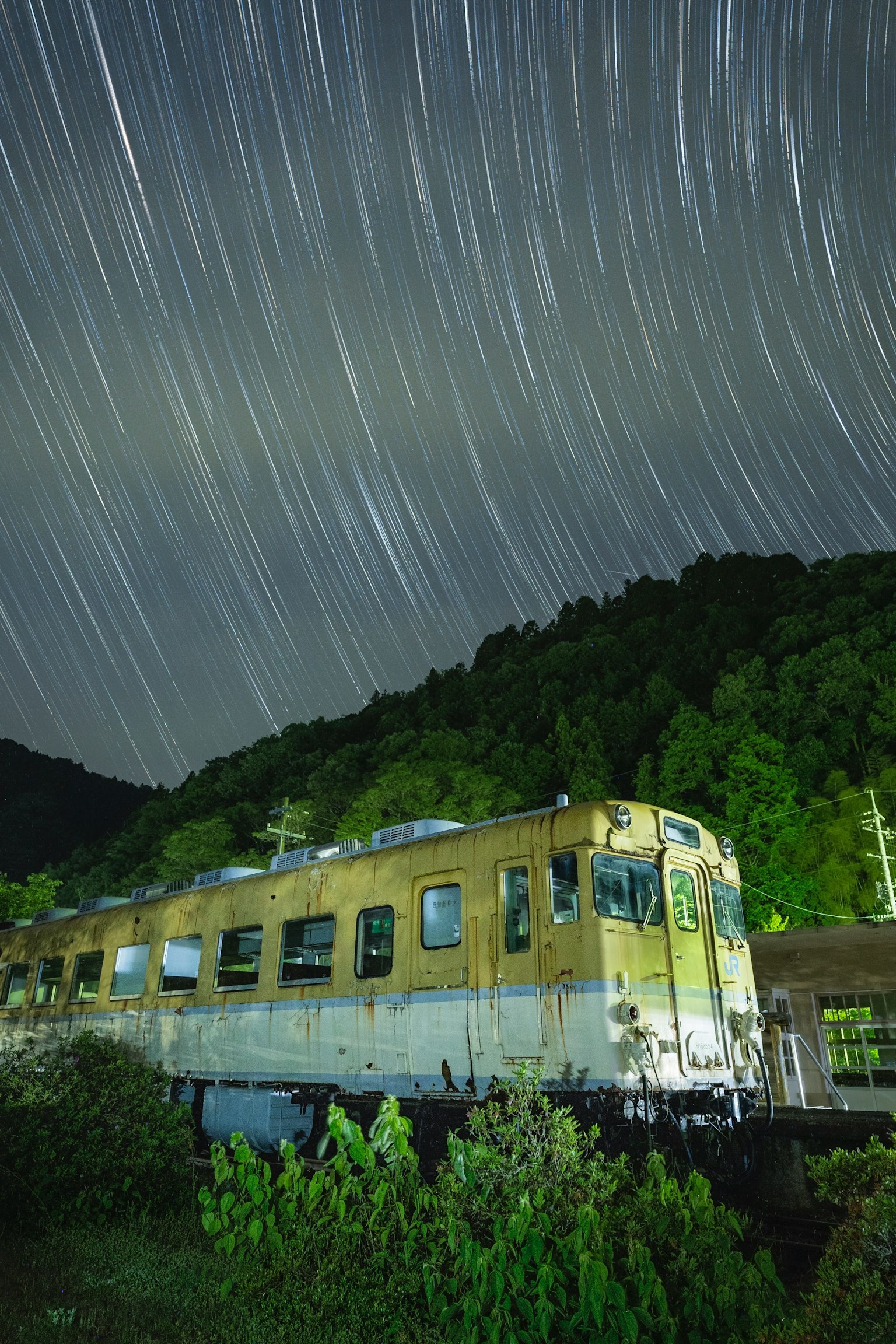 Un vecchio treno sotto un cielo stellato con scie di stelle e montagne verdi