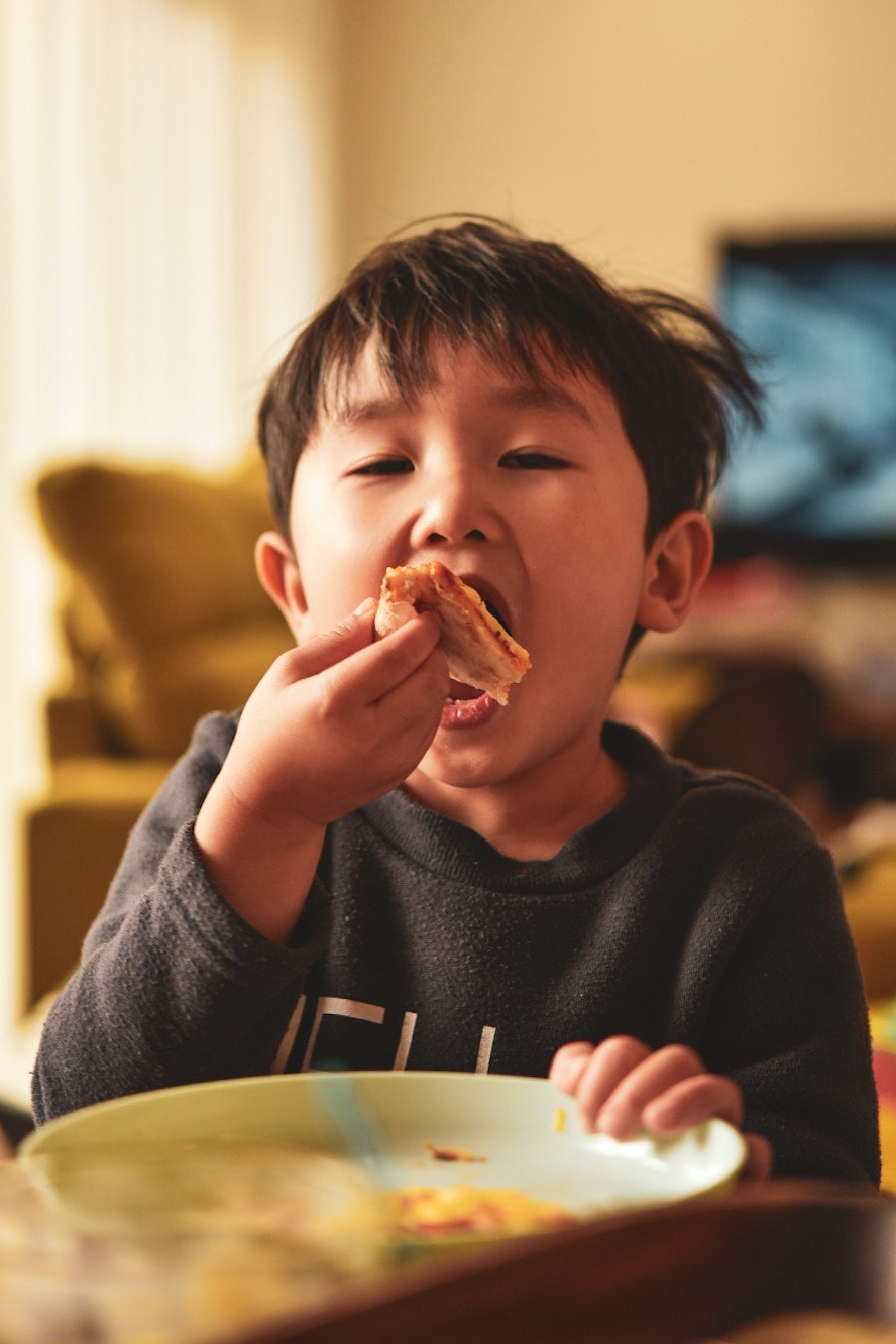 Un enfant aux cheveux en bataille mangeant une pizza à table à la maison