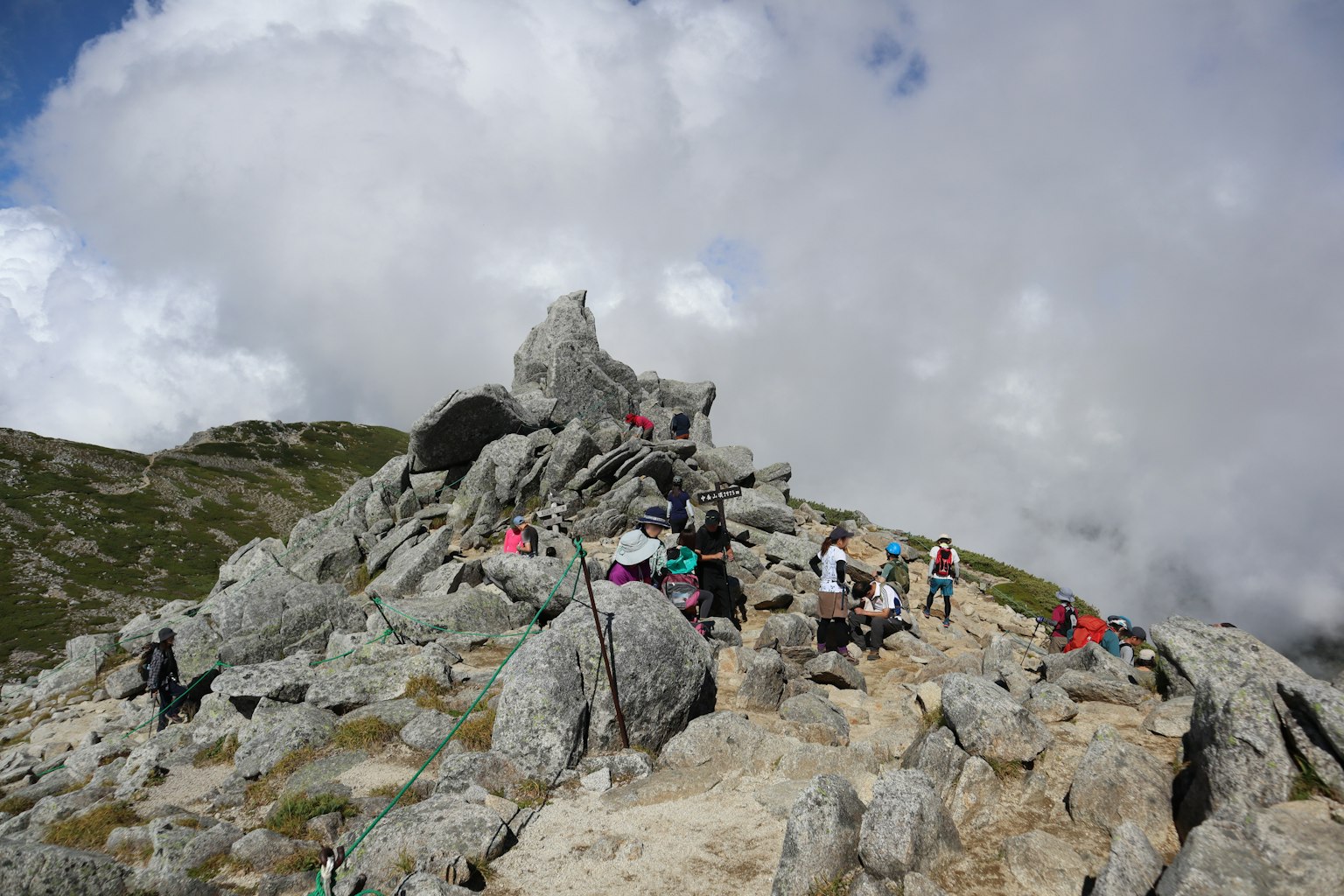 登山者在岩石山頂聚集，背景有雲層