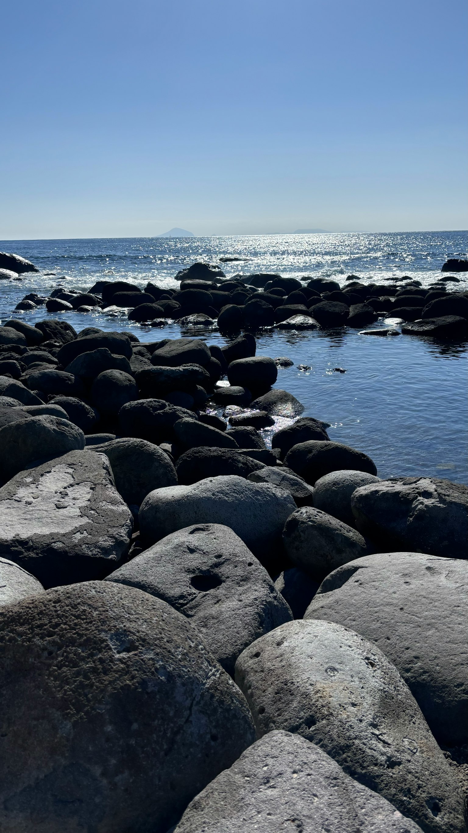 Garis pantai berbatu dengan ombak tenang dan langit biru yang jernih
