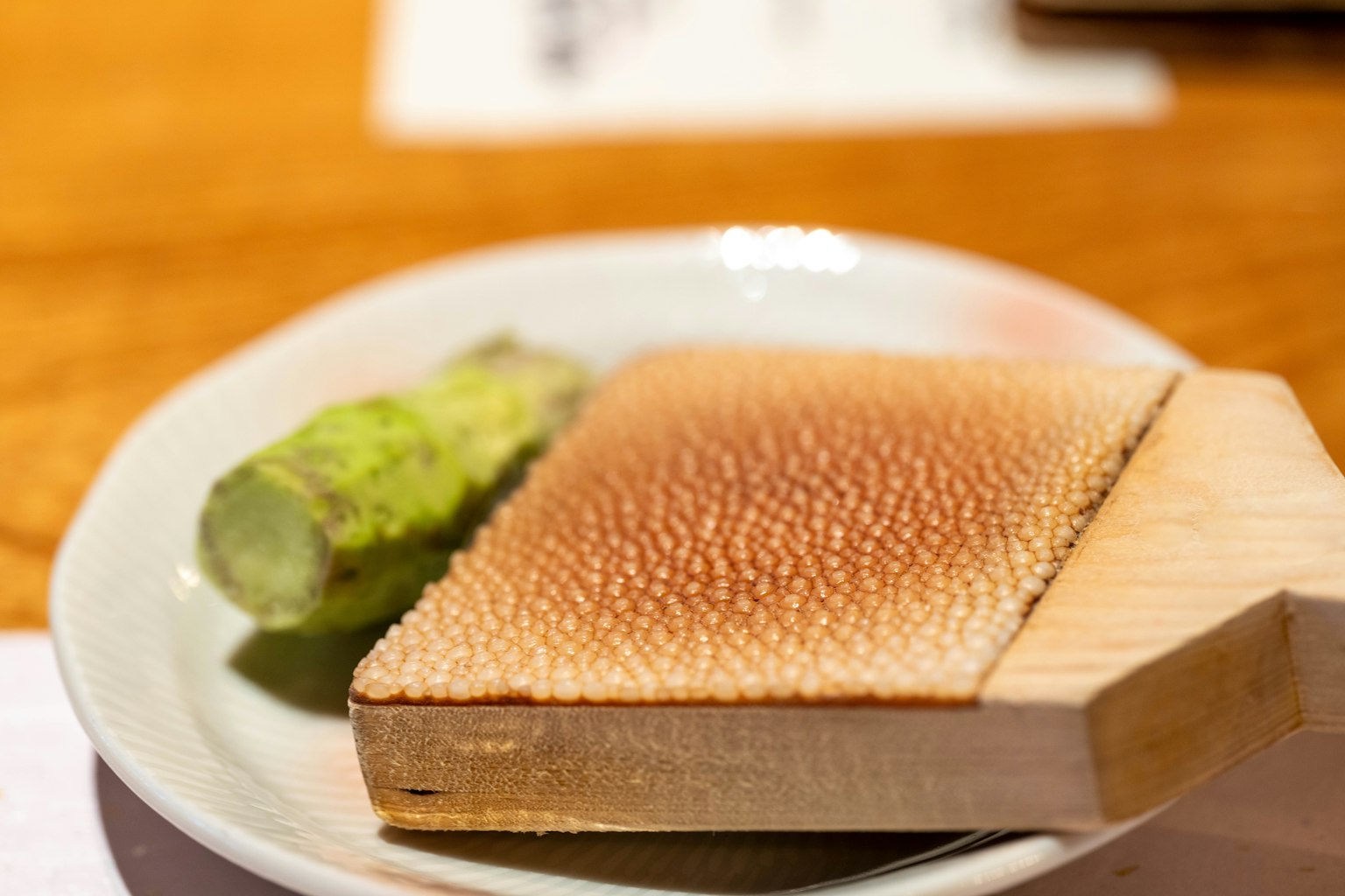 Grattugia di legno con superficie bruciata e un pezzo di wasabi su un piatto