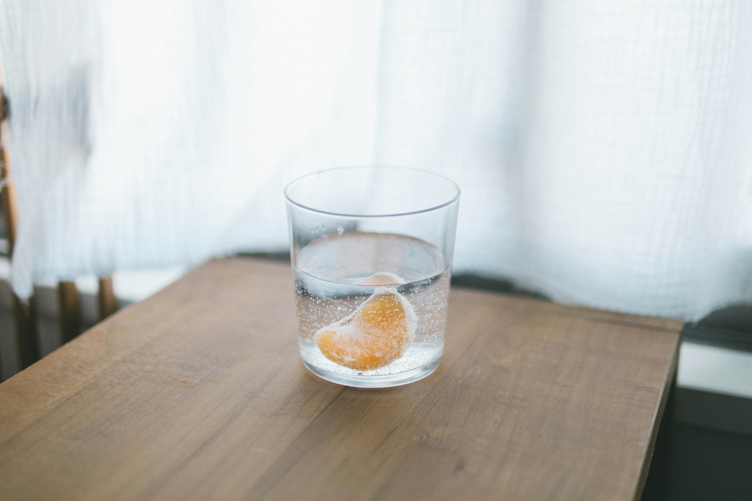 A clear glass with water and a slice of orange on a wooden table